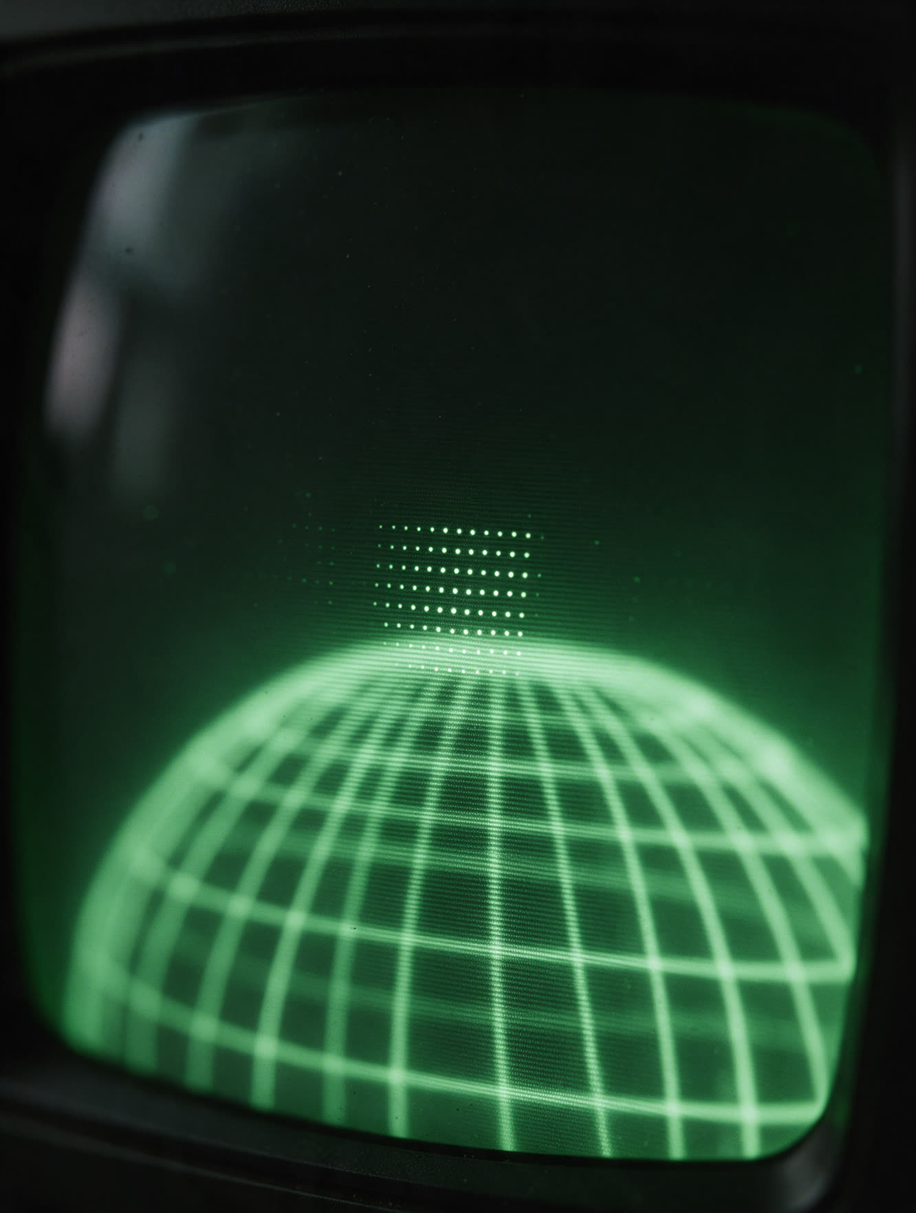 A close photograph of a green phosphor screen, scanlines sharp at the centre and softening toward the glass edge.